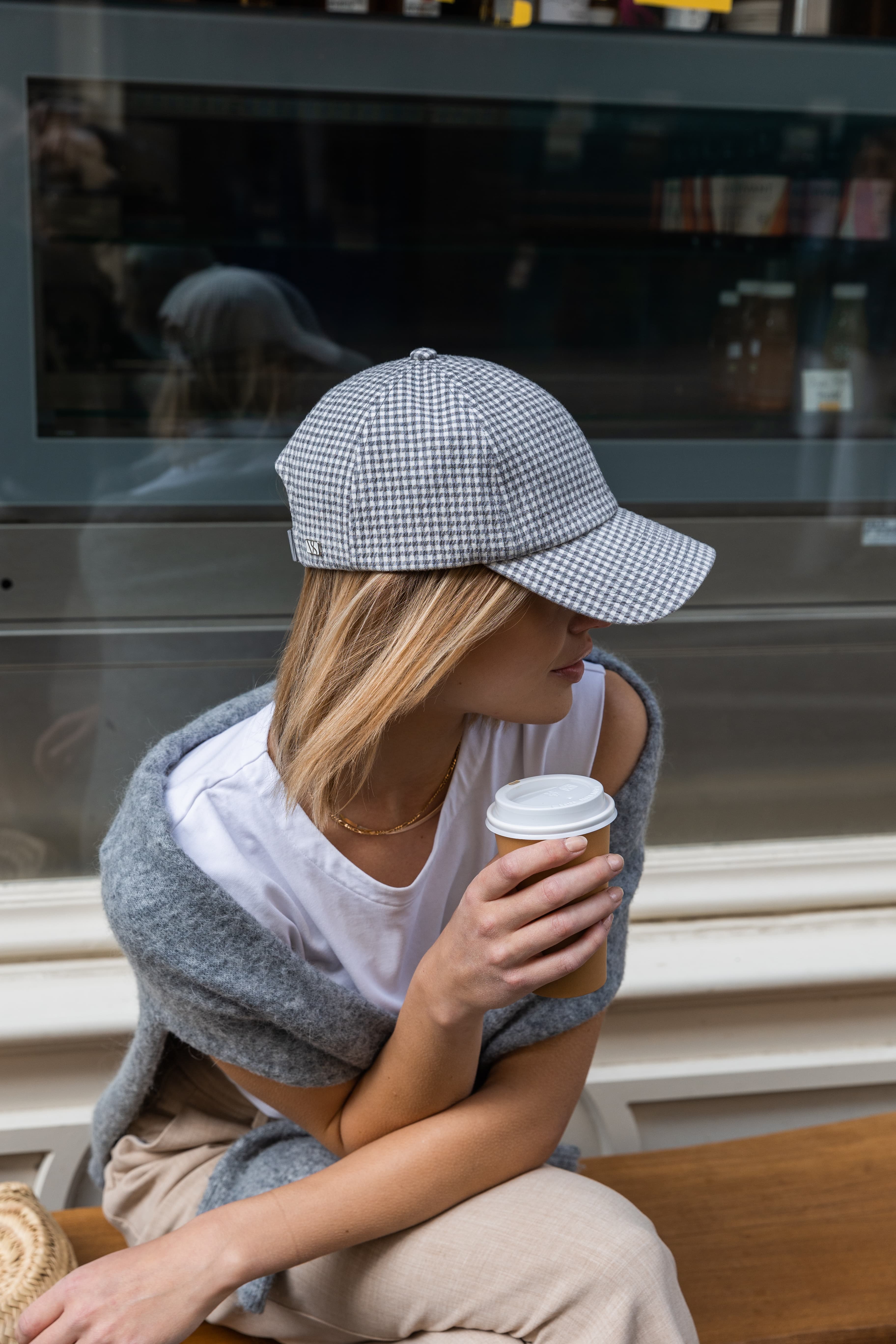 Side view of a female model wearing a grey seersucker cap while drinking coffee