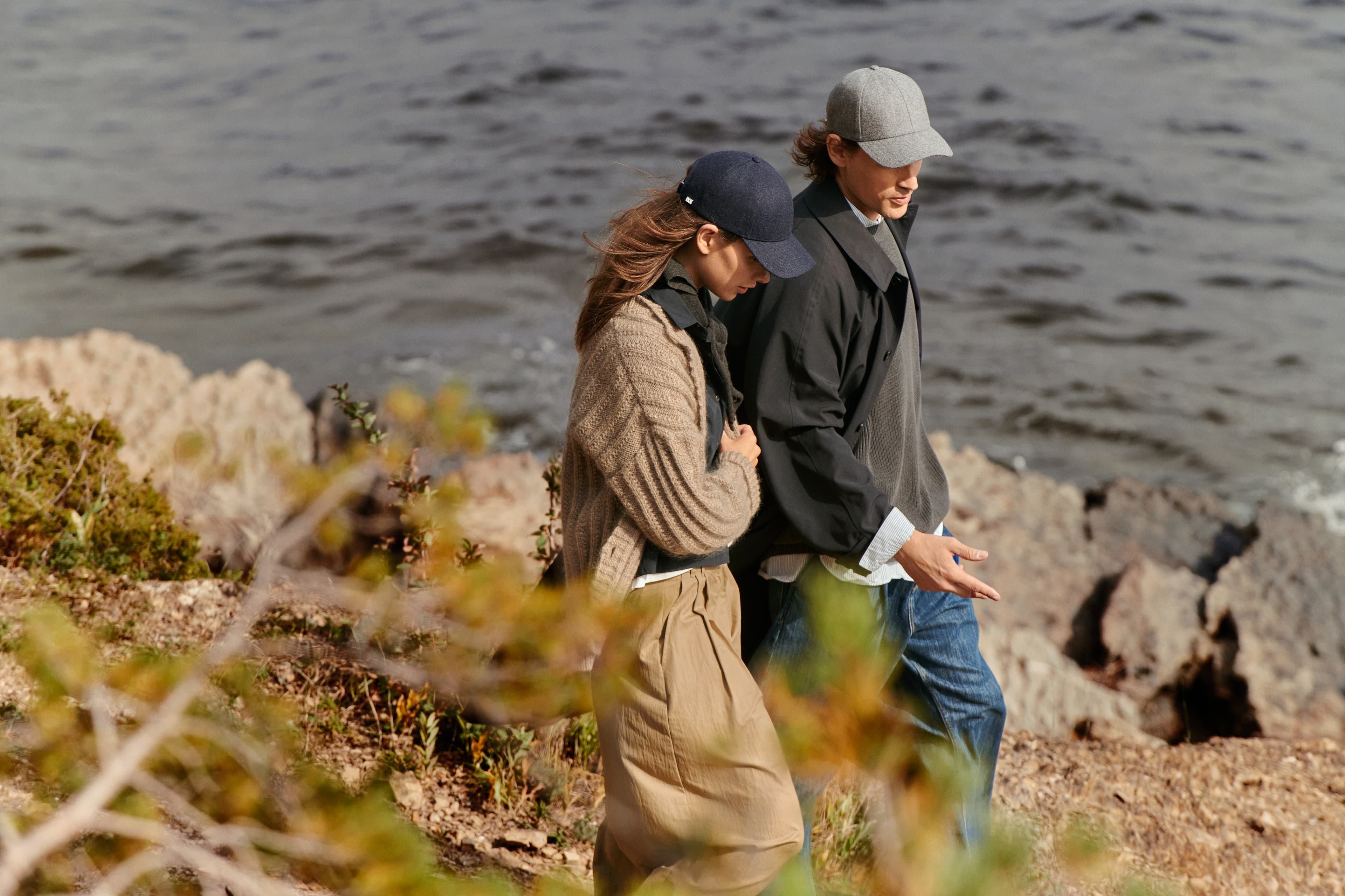 Side view of female and male model wearing a dark navy and grey wool cap by the ocean