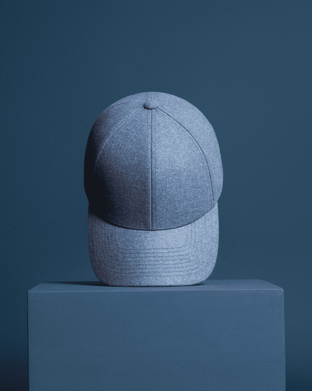 blue baseball cap displayed on a matching pedestal against a solid blue background.
