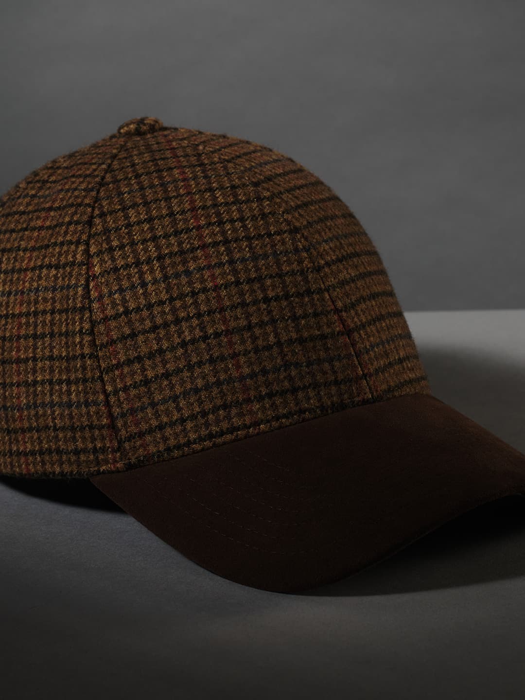 A brown checkered baseball cap with a dark brim, on a dark gray background.