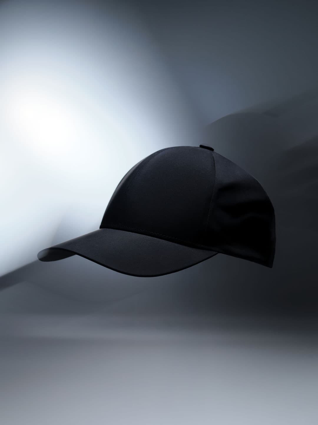 Side view of a black baseball cap floating in a dimly lit, abstract space with a soft gradient background.