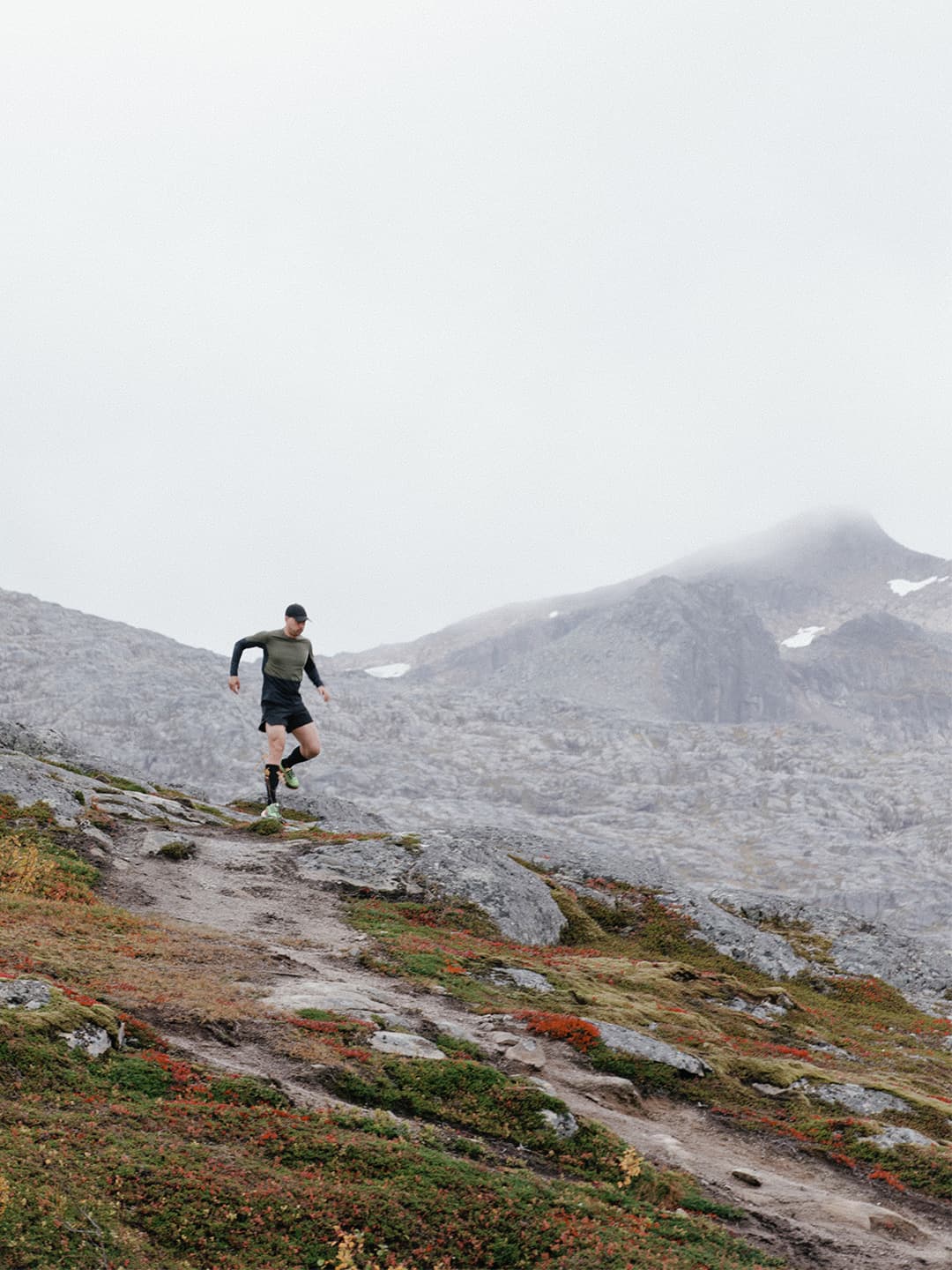 A person runs down a rocky mountain trail, surrounded by misty peaks and sparse vegetation.
