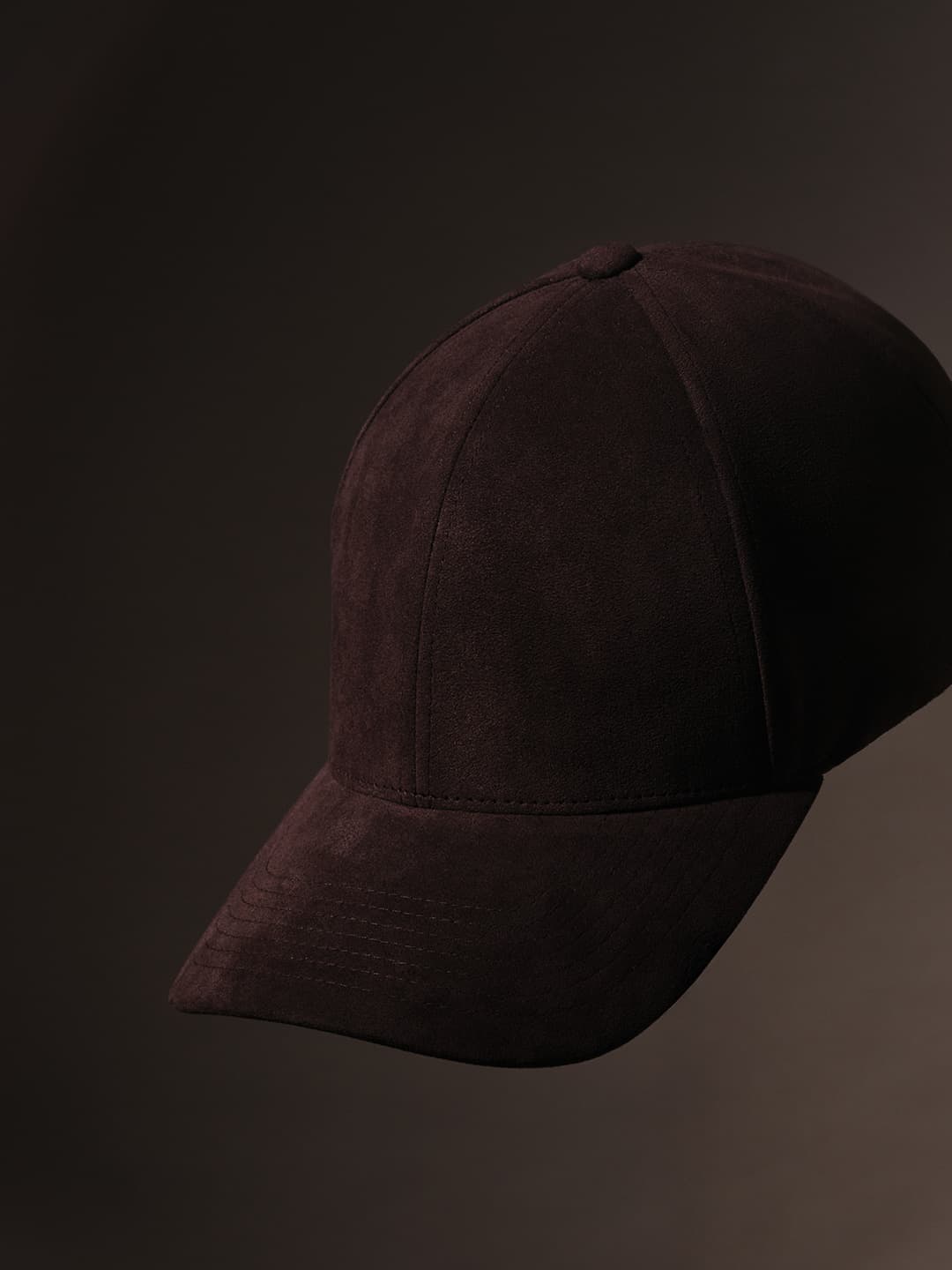 A dark brown suede baseball cap against a dark background, showcasing its textured fabric and curved brim.