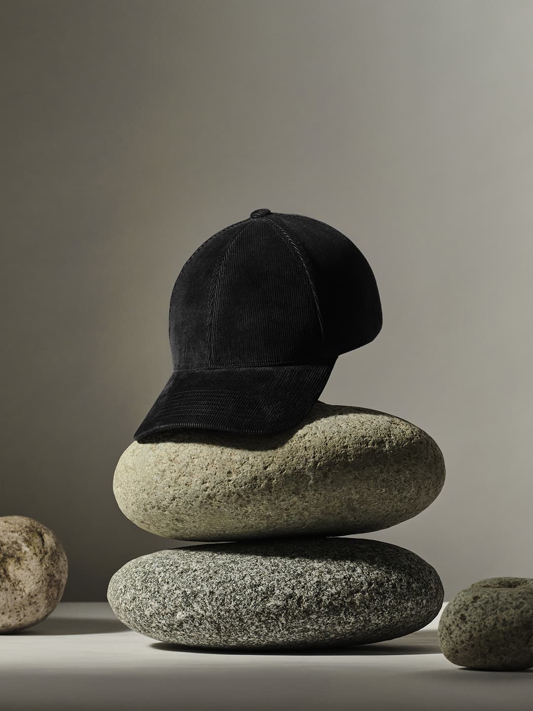 A black cap rests on two stacked smooth stones against a simple, neutral background.