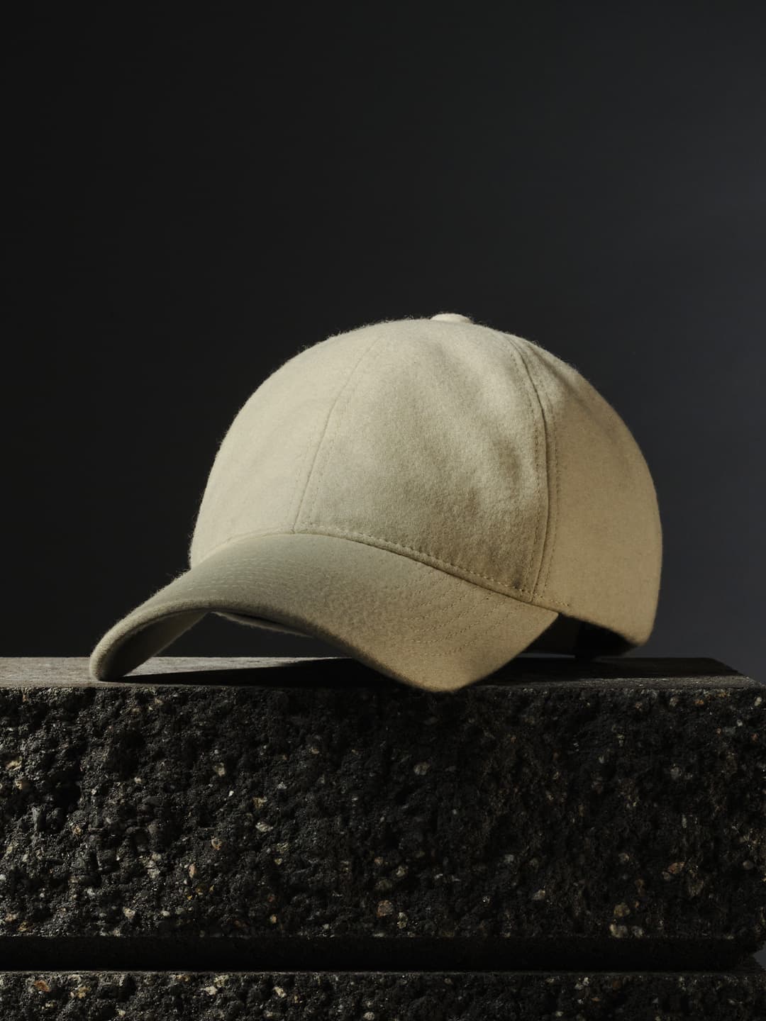 A snow white baseball cap resting on a textured black stone surface against a dark background.