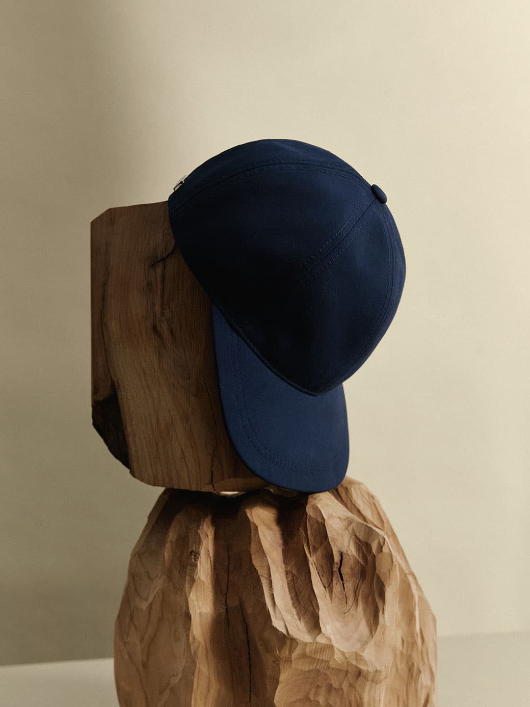 A navy blue baseball cap displayed on a sculpted wooden block against a beige background.