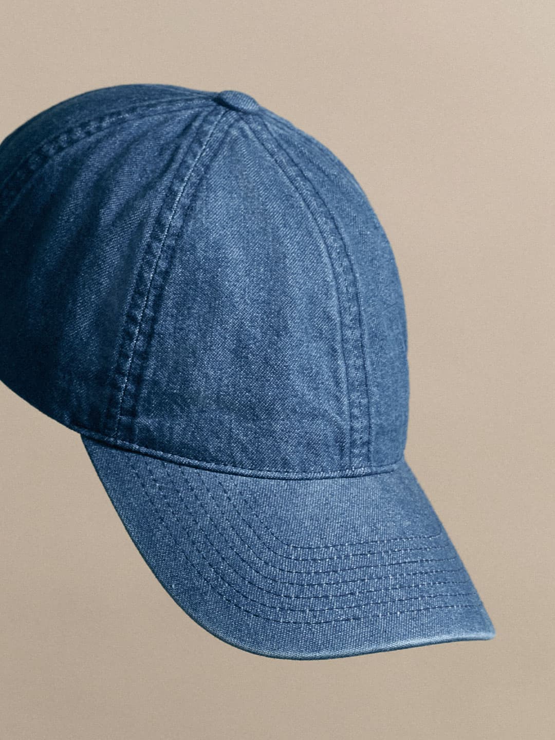 A blue denim baseball cap with visible stitching, set against a plain beige background.