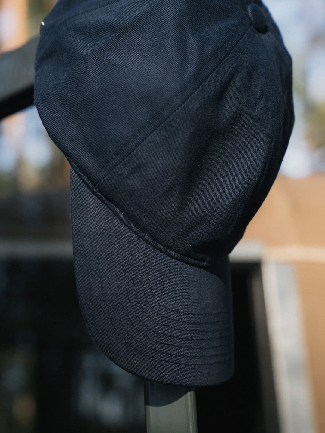 A navy blue baseball cap hanging on a rail with a blurred outdoor background.
