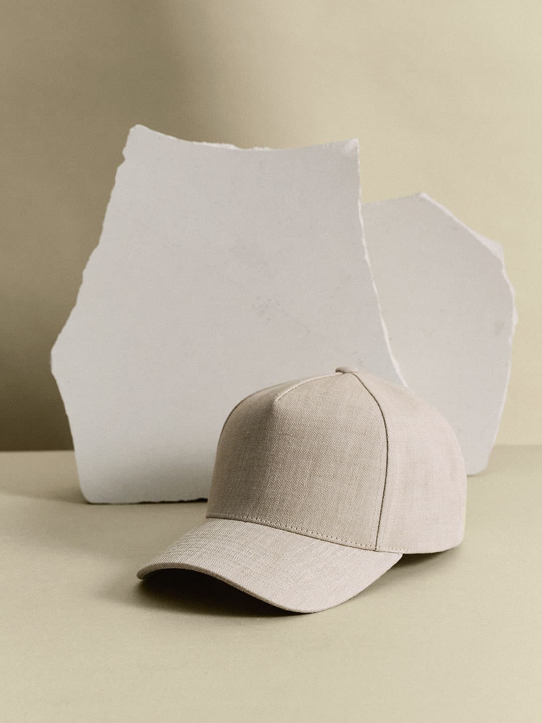 A beige baseball cap is placed in front of two irregularly shaped white slabs against a neutral background.
