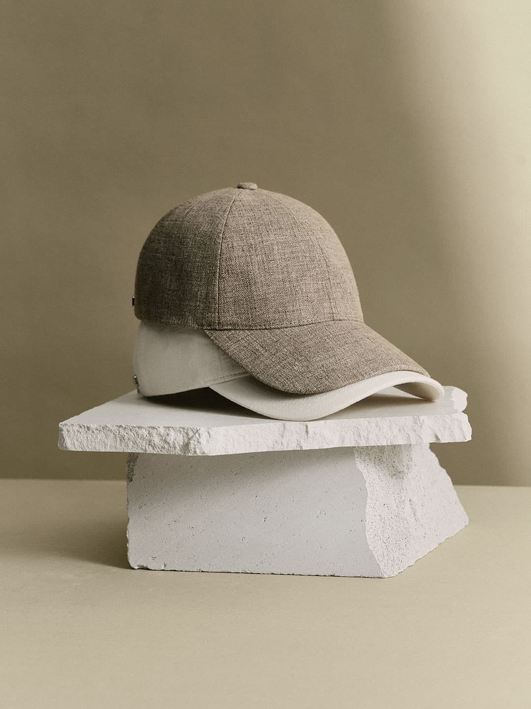 Beige baseball cap on a broken white concrete slab, against a plain beige background.