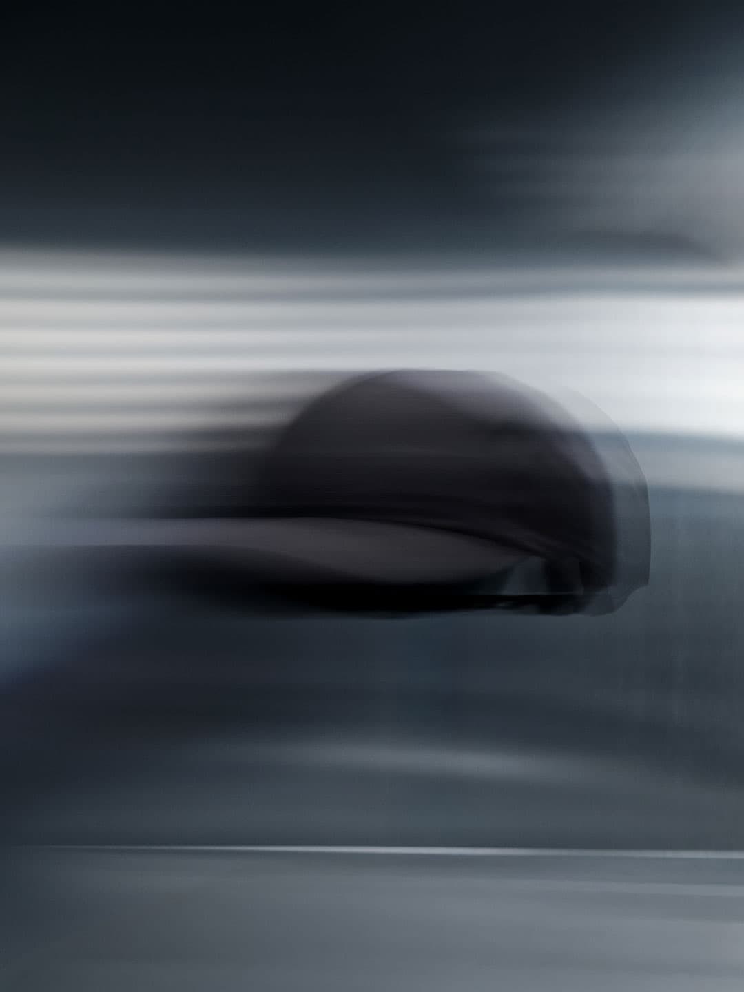 A blurred, dark cap appears to be moving swiftly against a gradient background of gray and white, creating a sense of motion and speed.