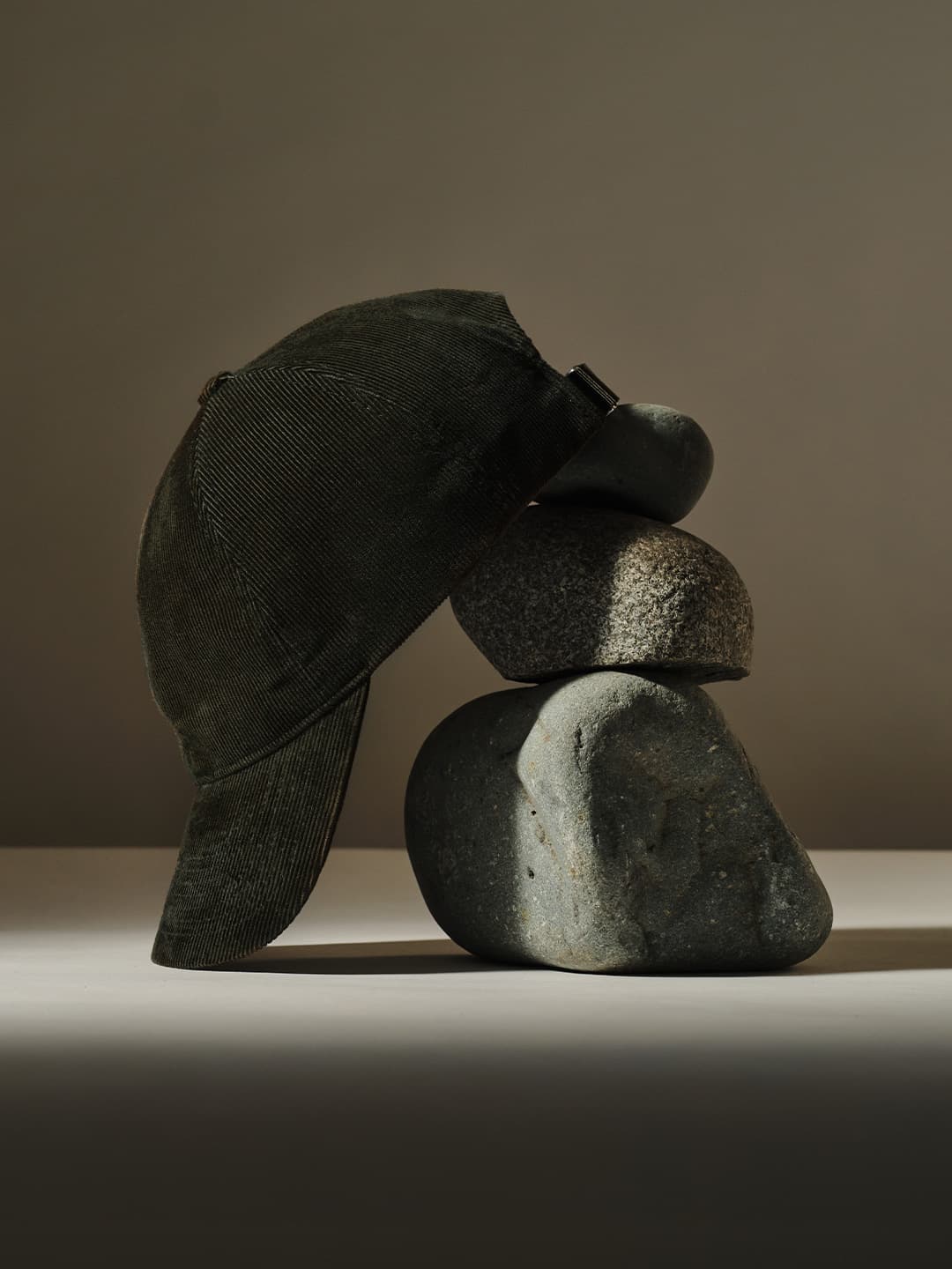 A dark green cap balanced on top of a stack of smooth, grey stones against a plain background.