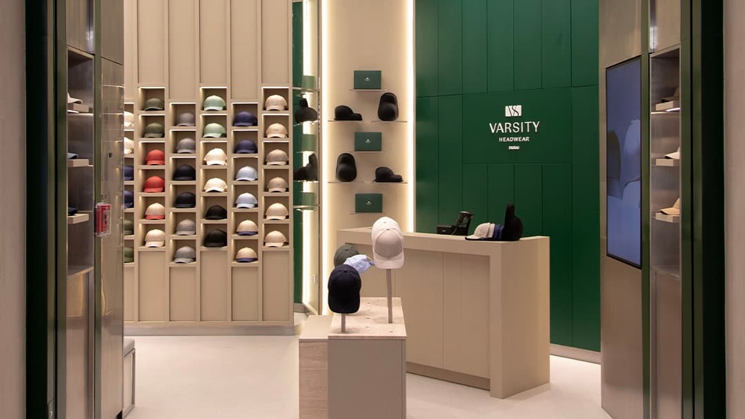 A modern store interior displaying various colorful caps on shelves, with a central counter beneath a "Varsity Headwear" sign.
