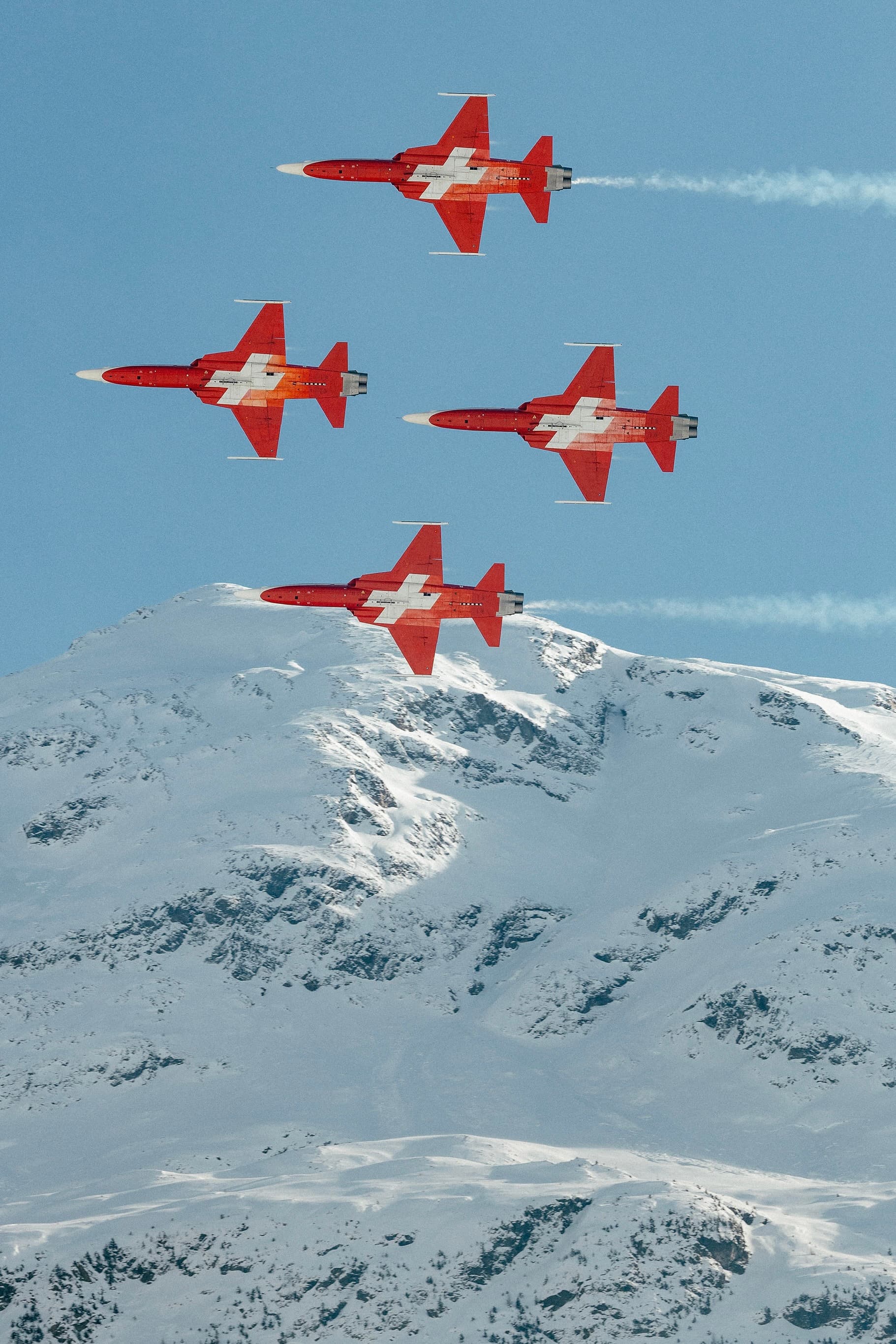 Five jets with the swiss flag in formation fly over snow-covered mountains under a clear blue sky at The I.C.E in St. Moritz