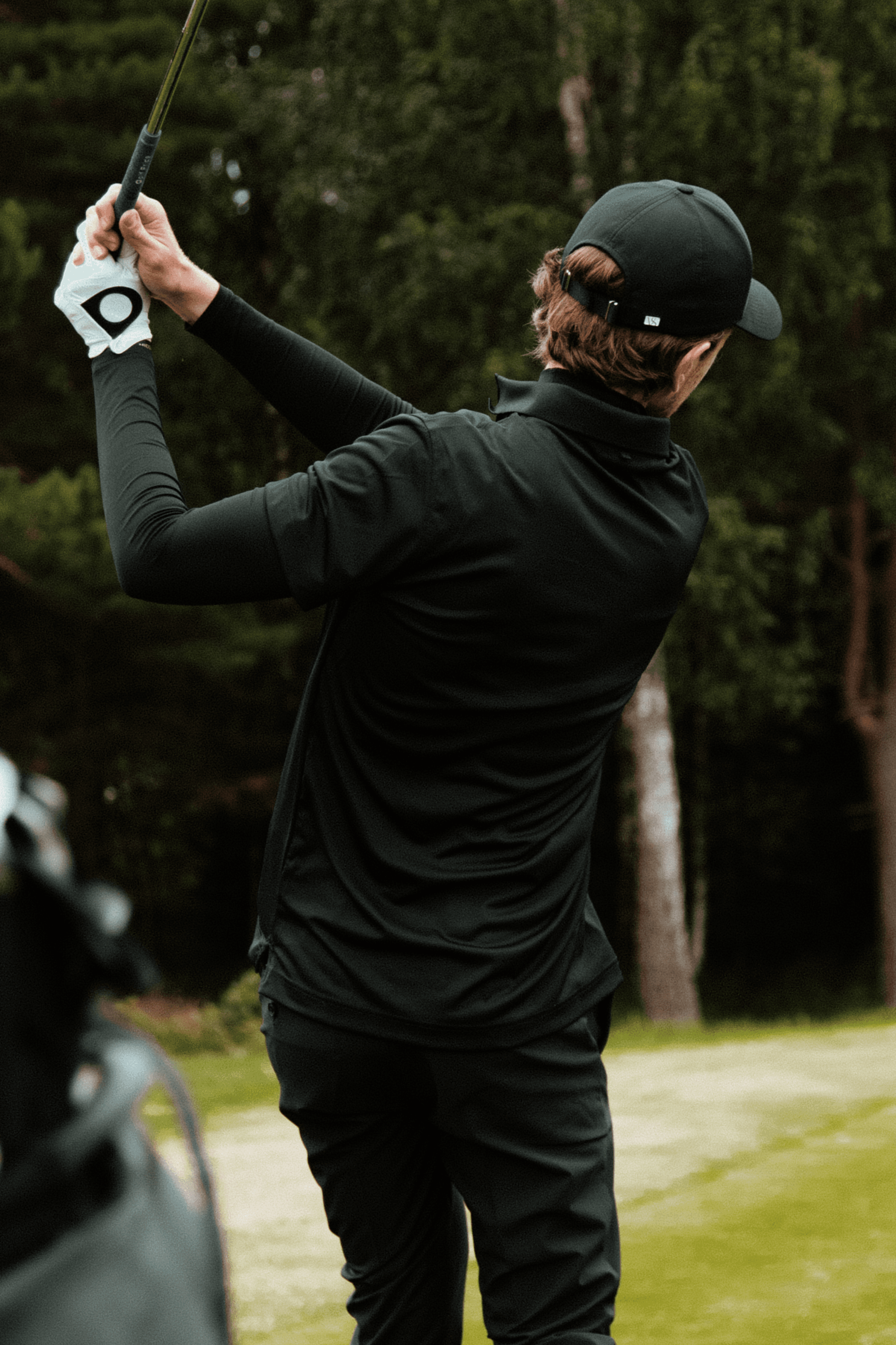 Back view of golfer wearing a black athletic sport cap from varsity headwear