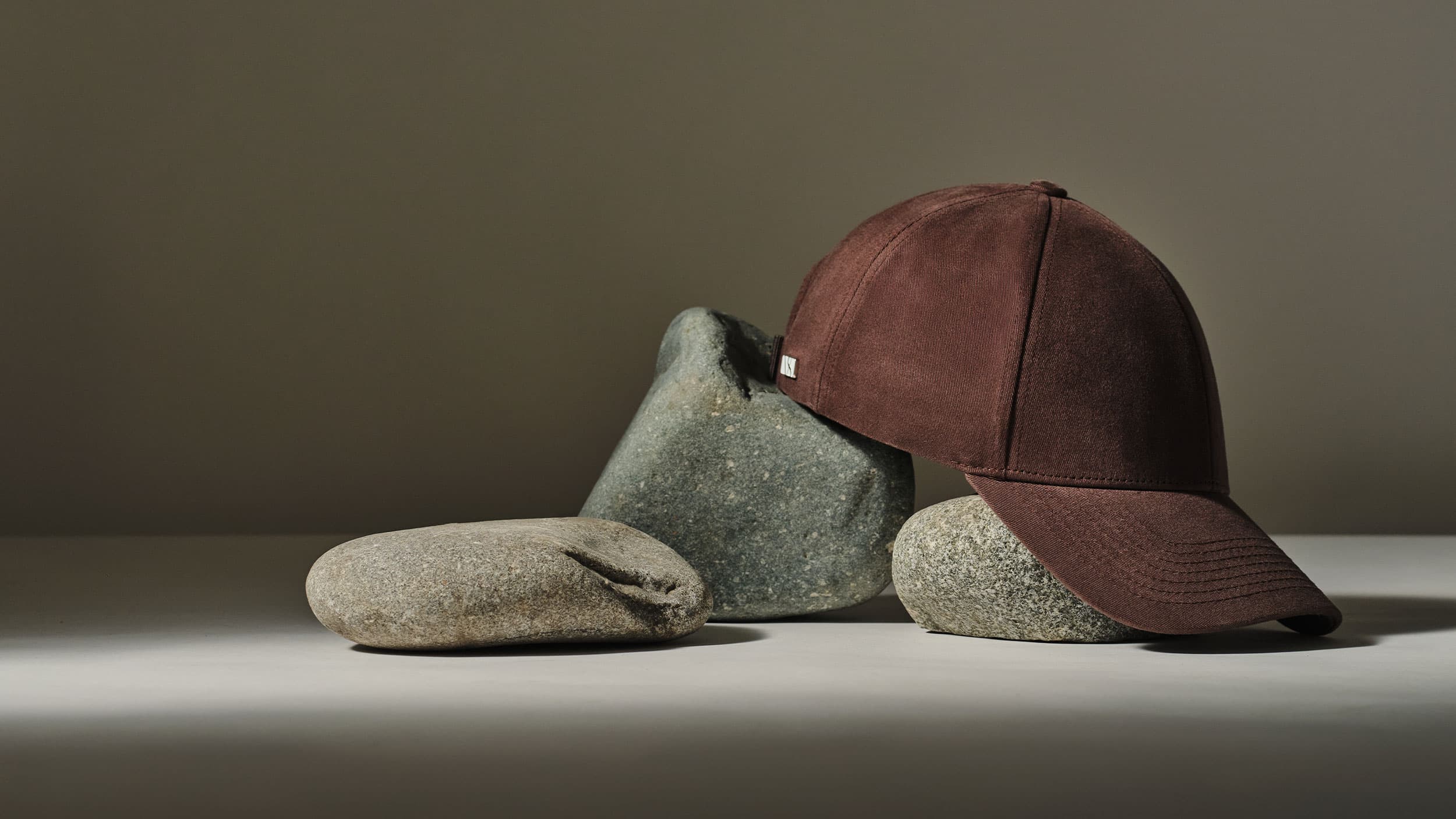 A brown baseball cap resting on several smooth, stacked stones against a plain background.
