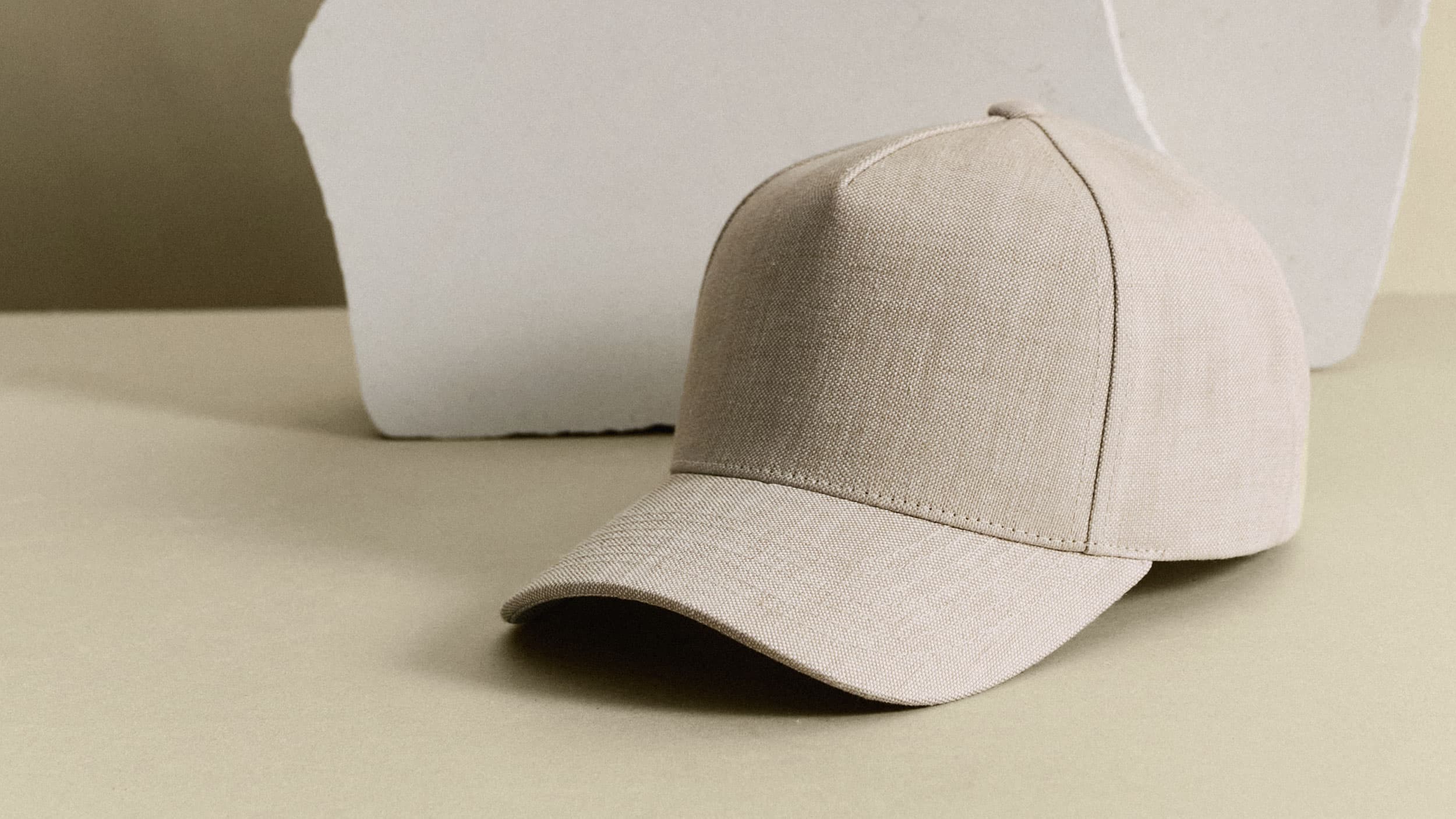 A beige baseball cap on a neutral background, with a piece of white textured material behind it.