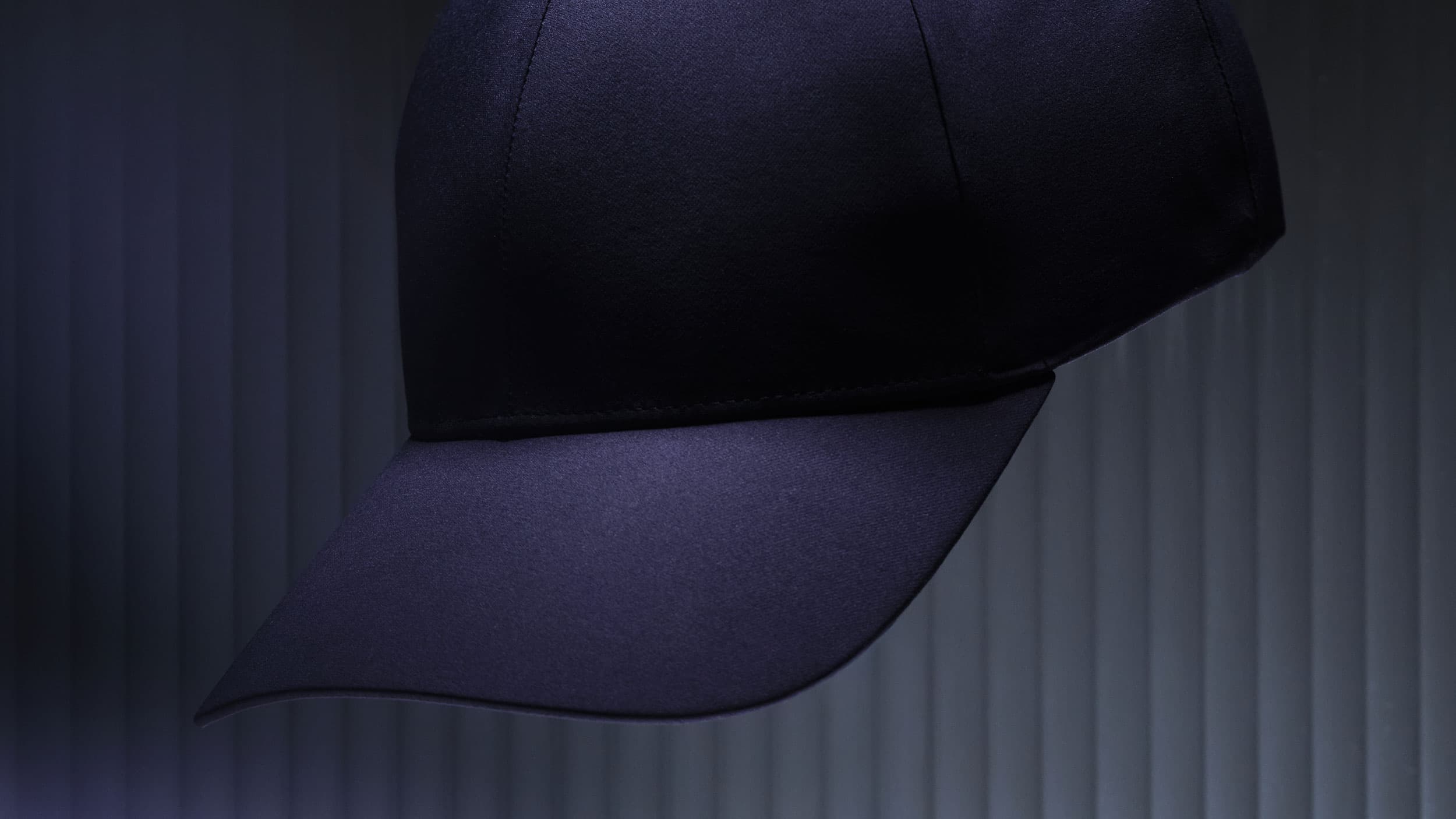 A dark blue baseball cap against a textured, vertical-lined background, illuminated with soft, dramatic lighting.