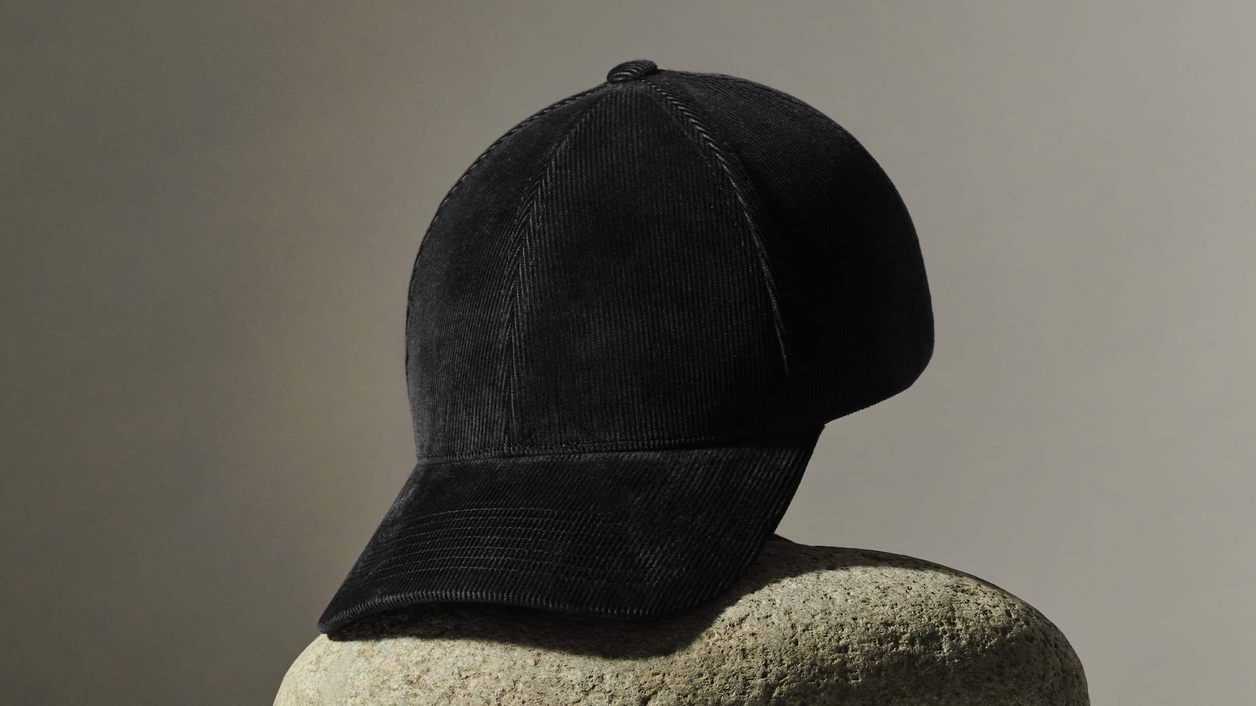 A black corduroy baseball cap resting on a textured stone surface with a neutral background.