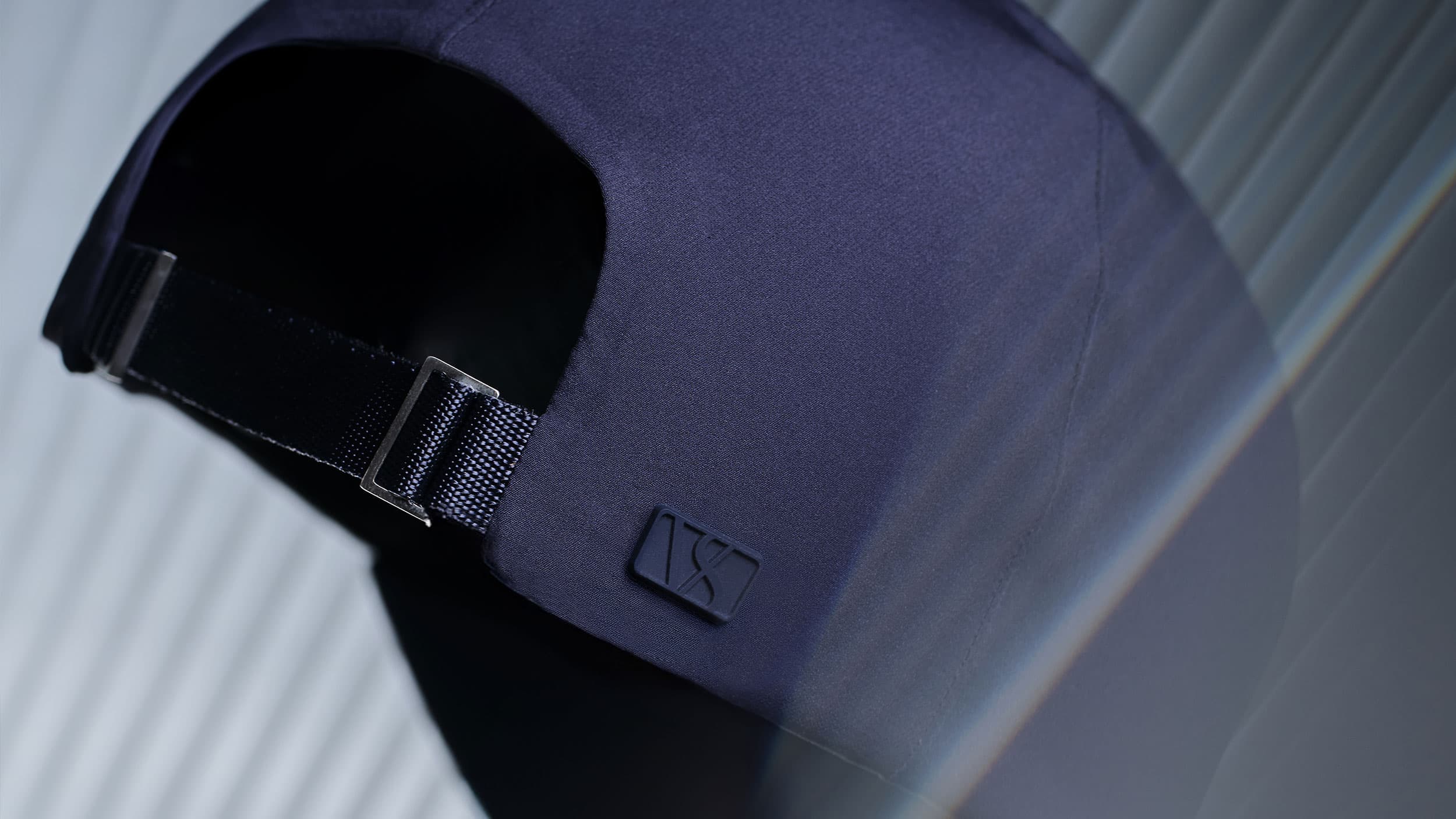 Close-up of a dark blue baseball cap showing the adjustable strap and a small logo on the side, against a softly focused background.