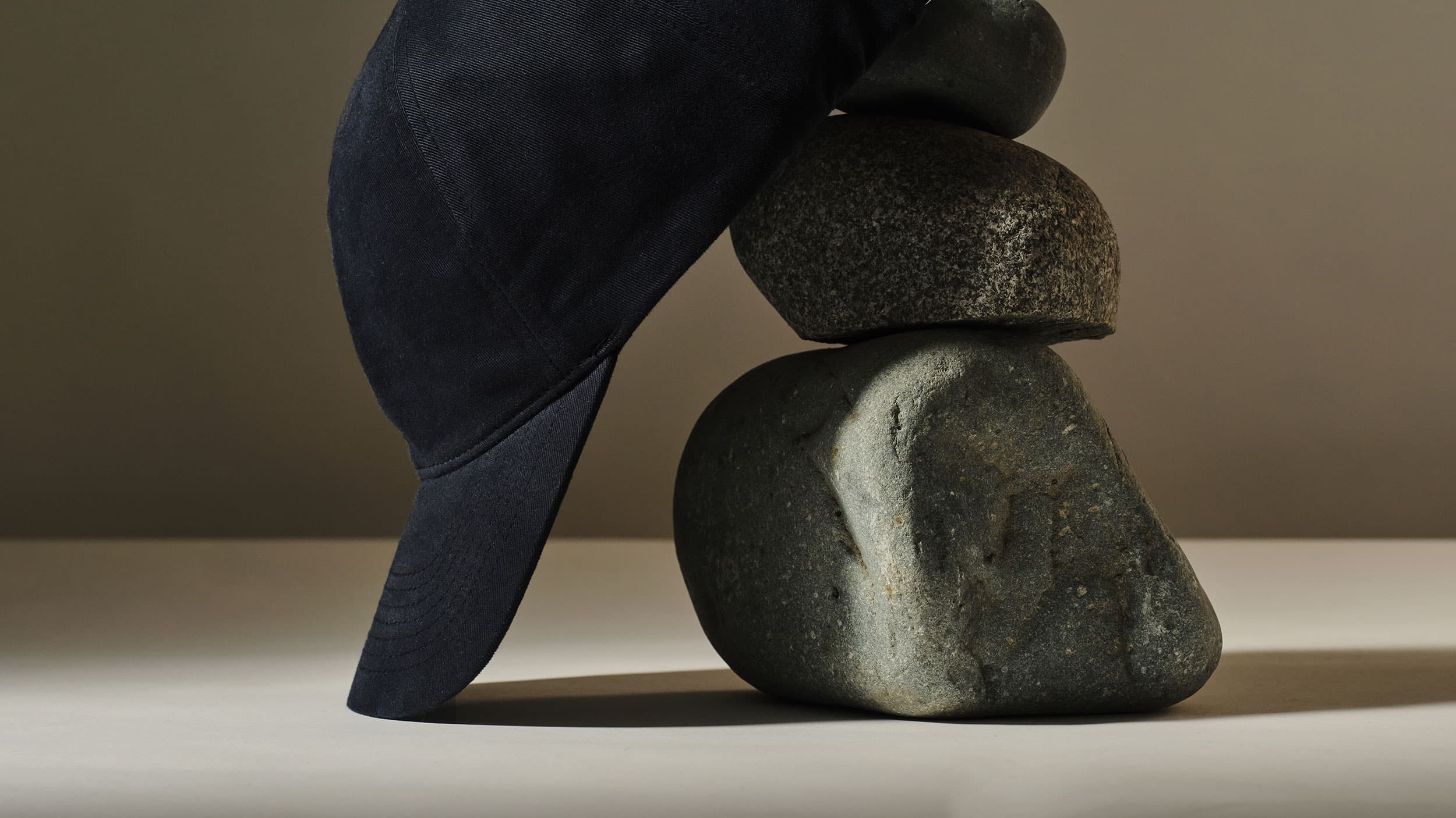 A black baseball cap is placed on top of a balanced stack of smooth gray stones against a muted background.