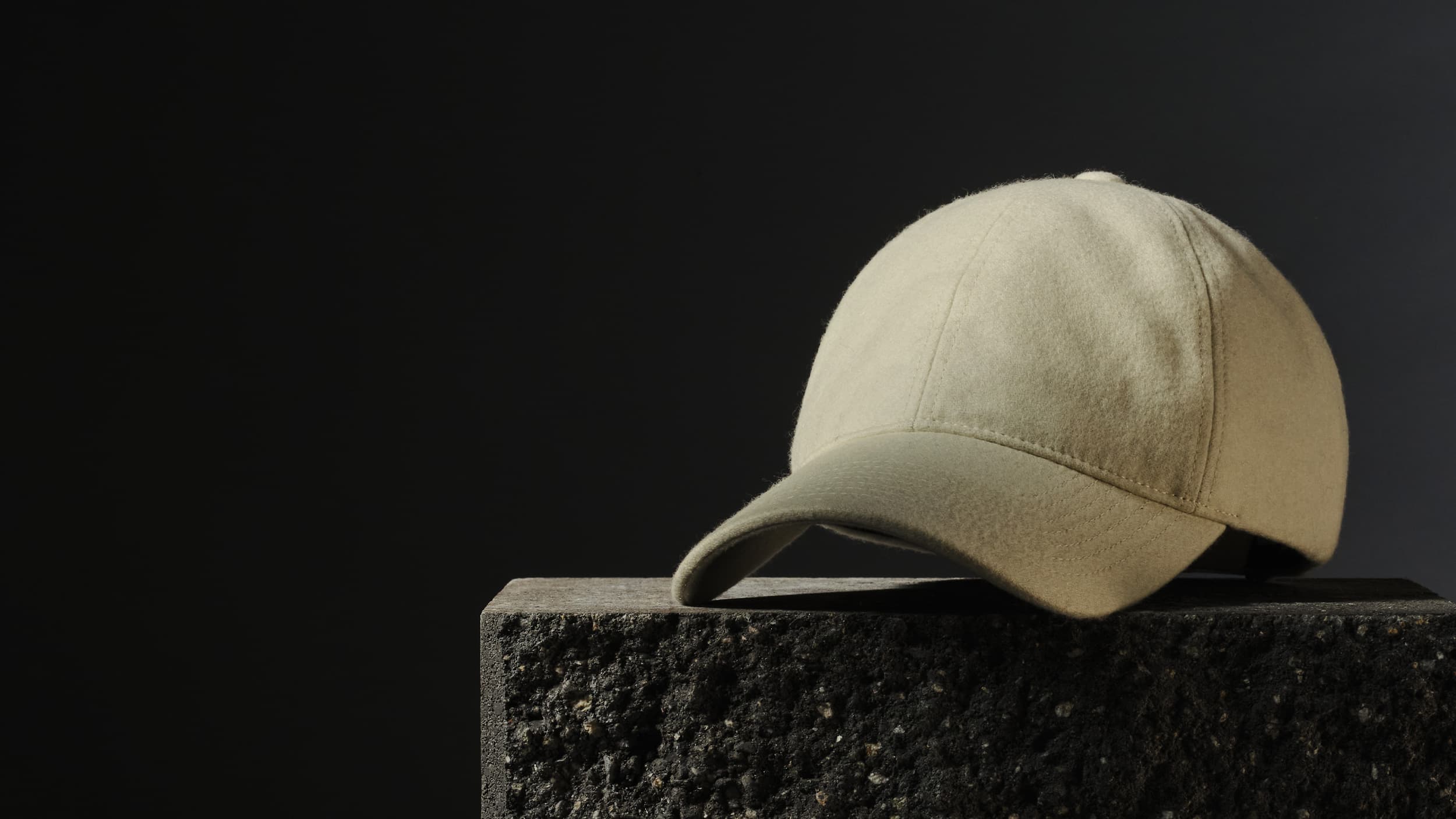 A beige baseball cap on a textured, dark stone surface against a black background.