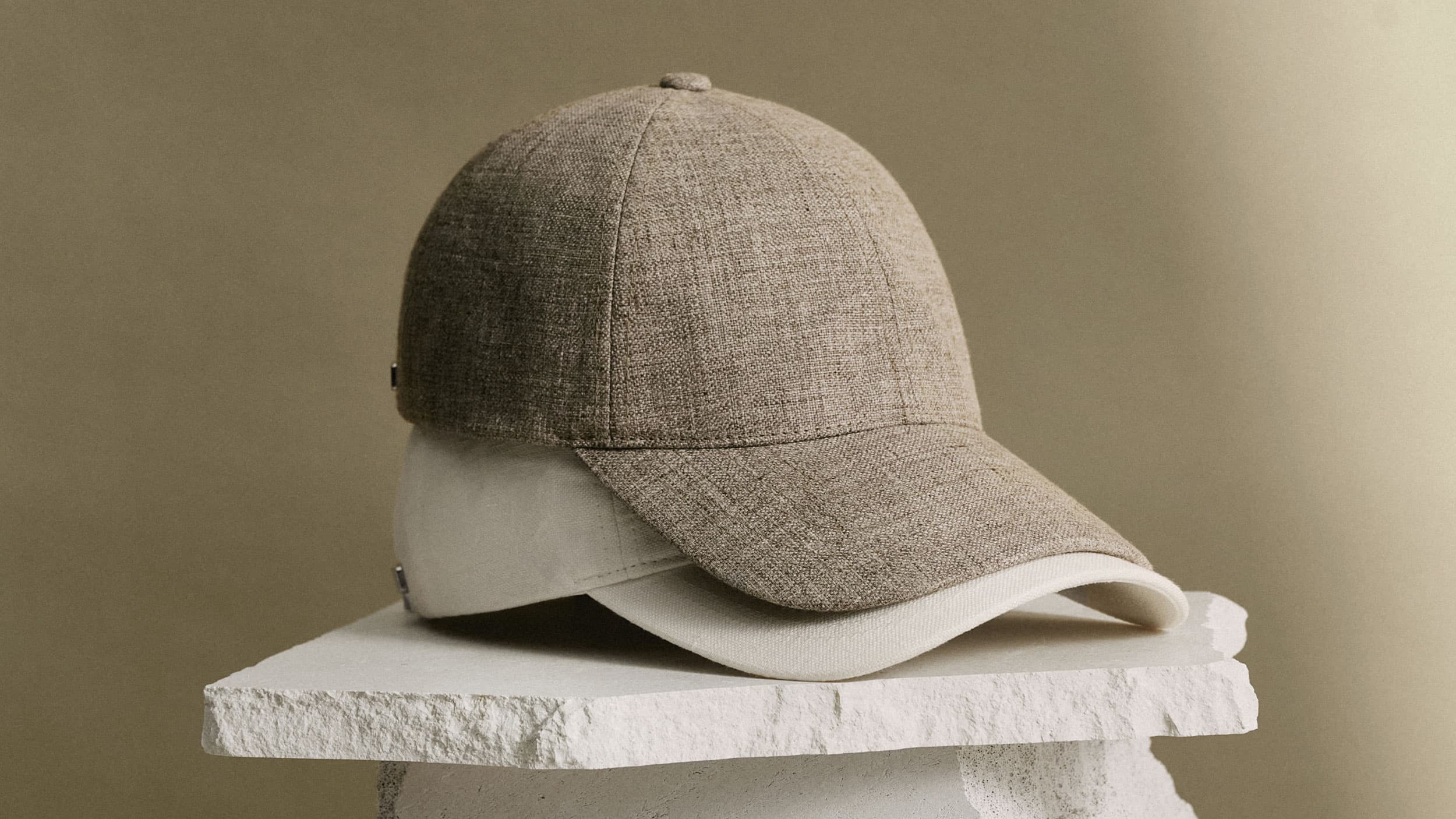 A beige linen cap on a white, rough stone surface against a neutral background.