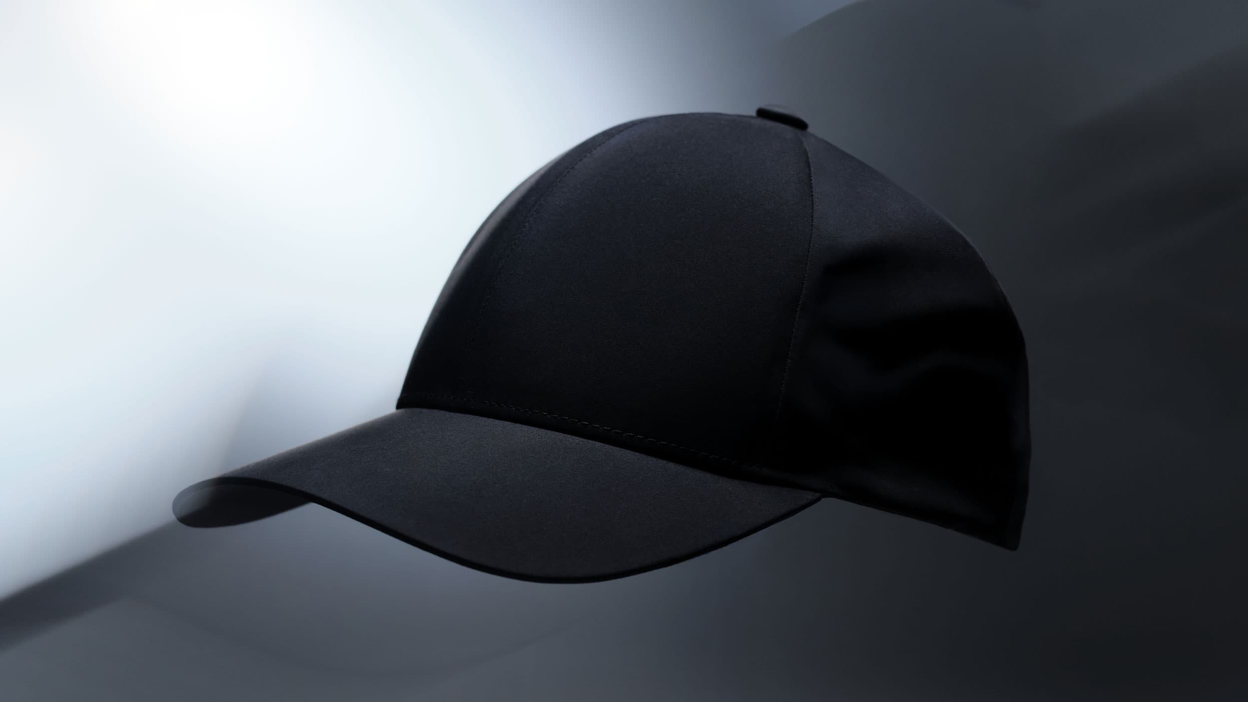 Side view of a black baseball cap with a curved brim against a blurred, monochromatic background.