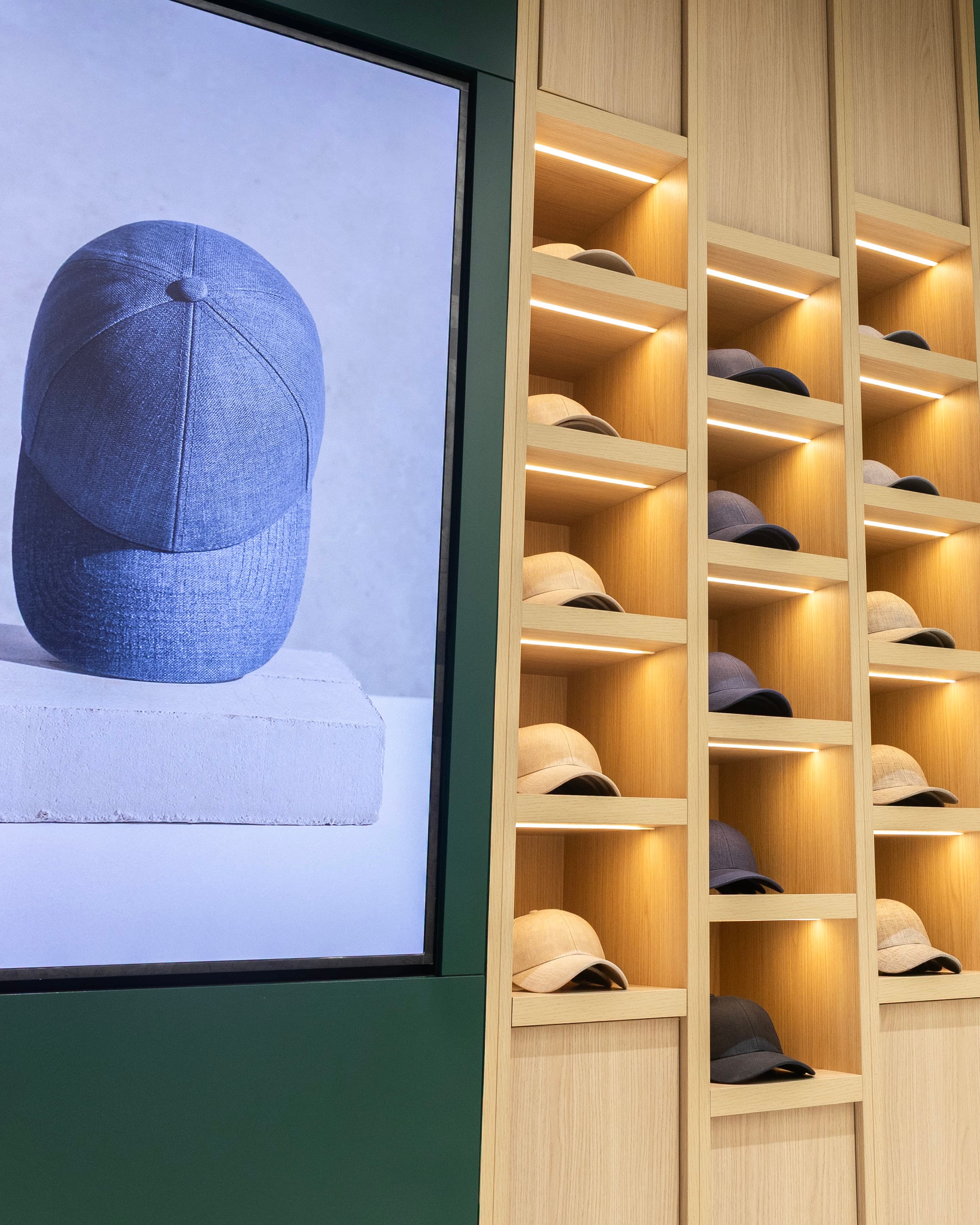 A display wall features shelves with neatly arranged caps in neutral colors, alongside a large digital sign showing a close-up of a gray cap.