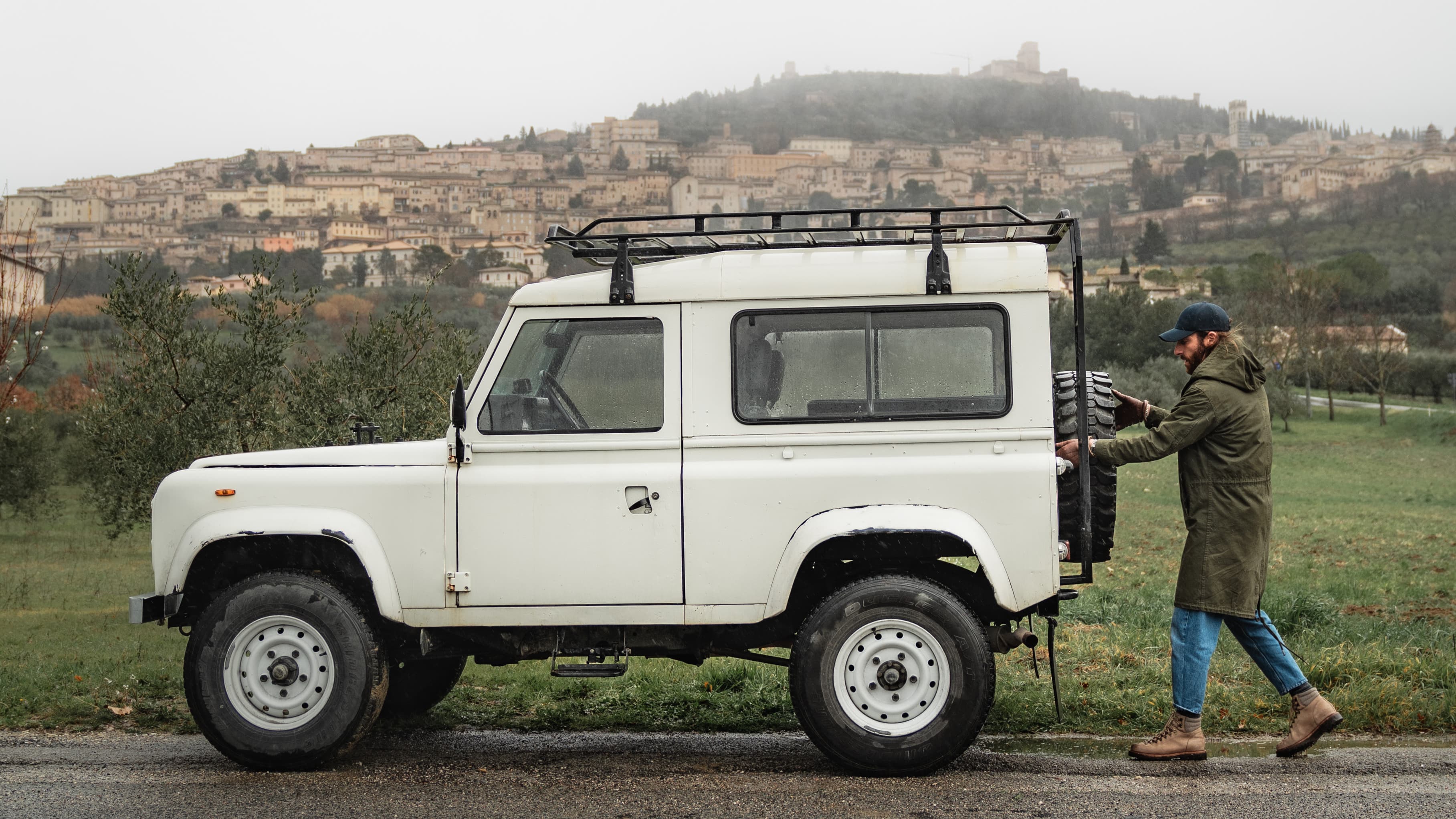 Side view of a lifestyle image with a white car and man wearing a dark blue varsity headwear cap