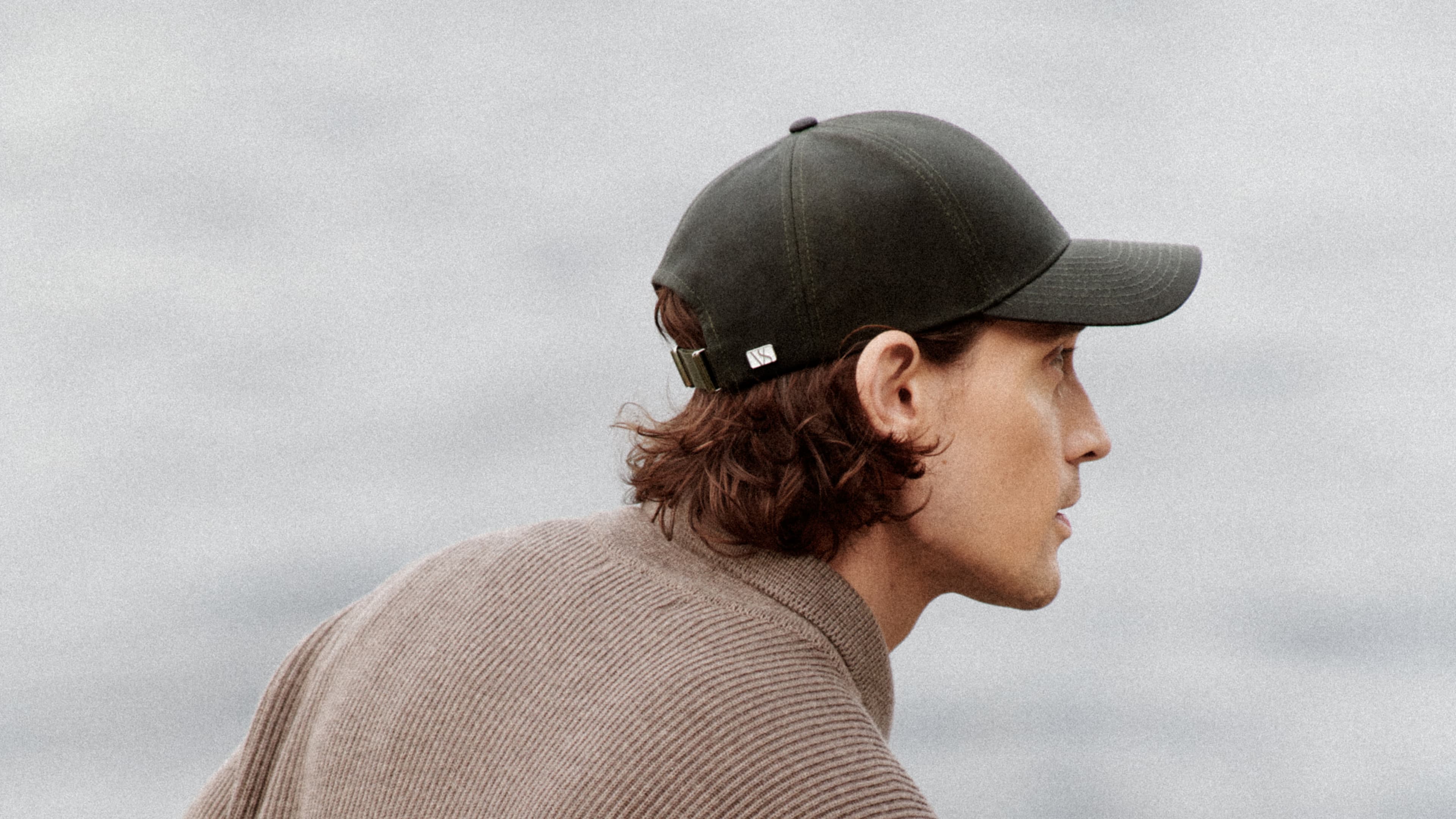 Side view of a male model wearing a green oilskin cap from varsity headwear