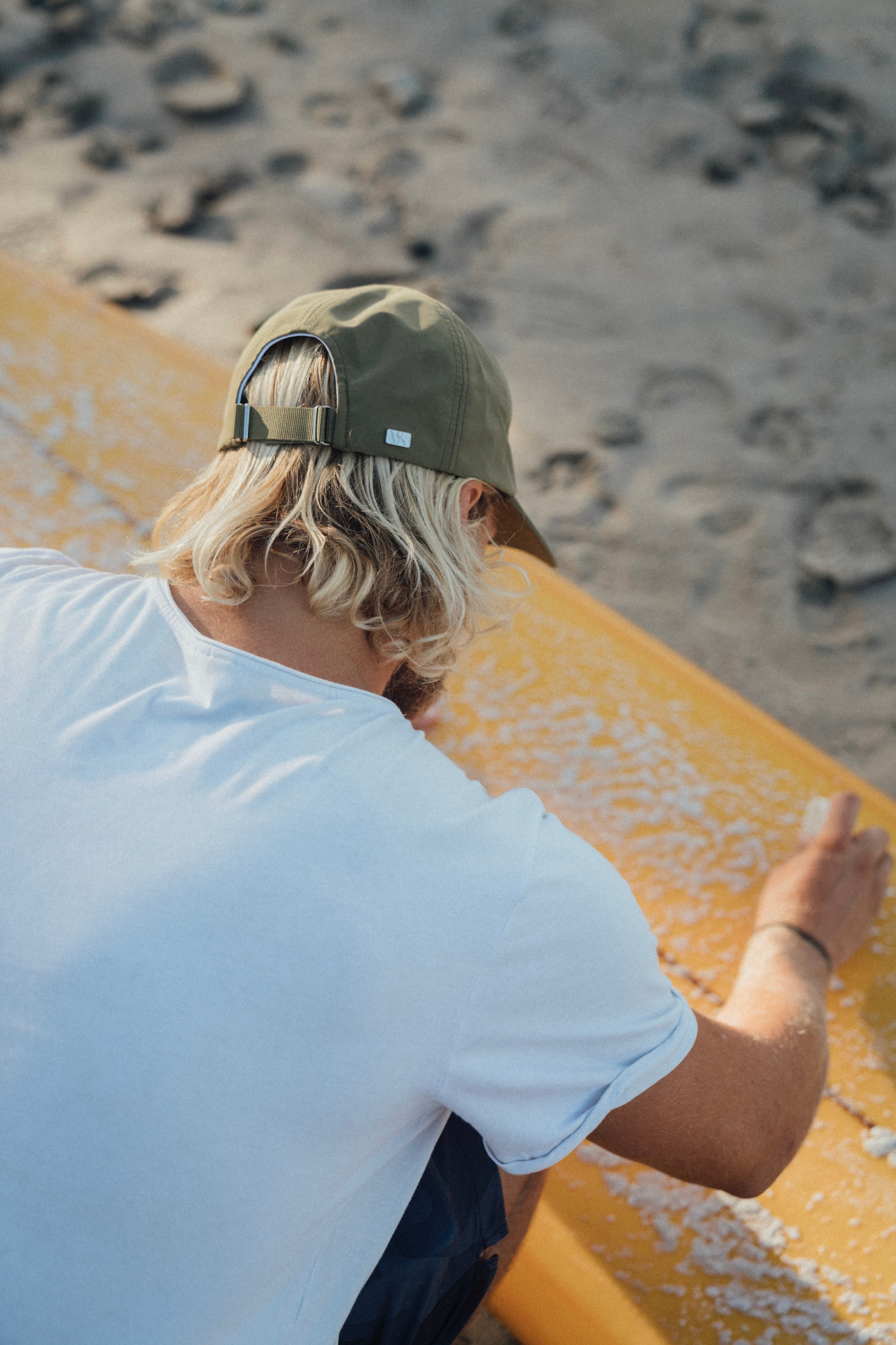 Surfer wearing seaqual cap while waxing surf board at the beach