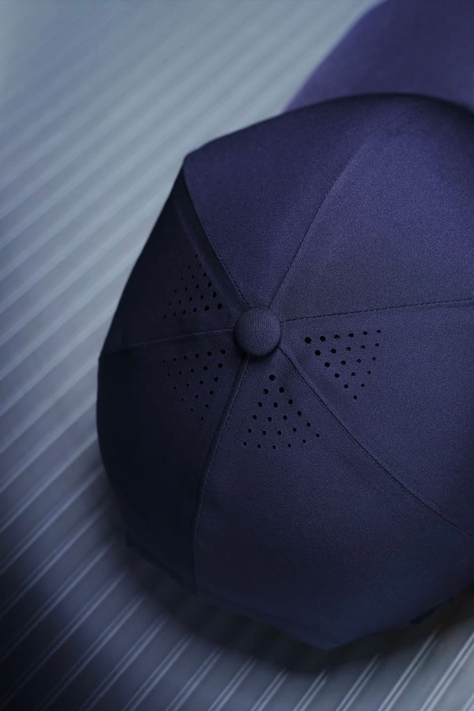 Close-up of a navy blue baseball cap with perforations on top, resting on a ribbed grey surface.
