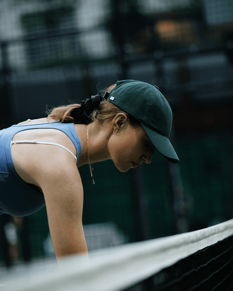 Side view of female model wearing a legacy soft cap while playing padel tennis