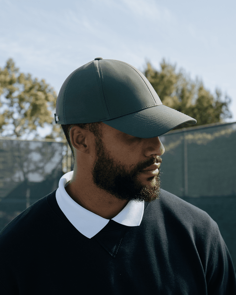 Side view of male model wearing a legacy structured athletic sport cap on tennis court